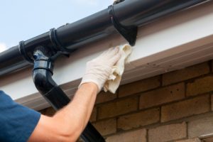 Bend employee cleaning gutter with a cloth and gloves on