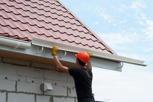 Bend worker gutter installation on a ladder with an orange hard hat on